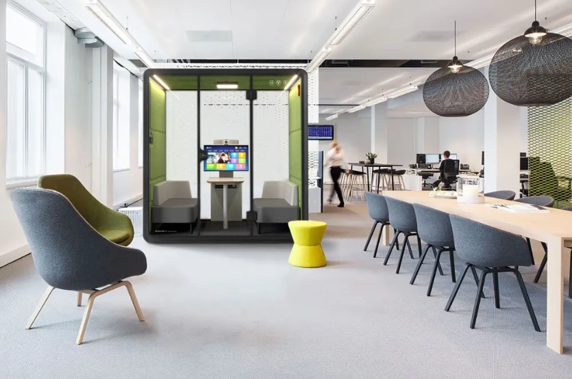 Acoustic meeting pod with a screen and seating in a modern open-plan office