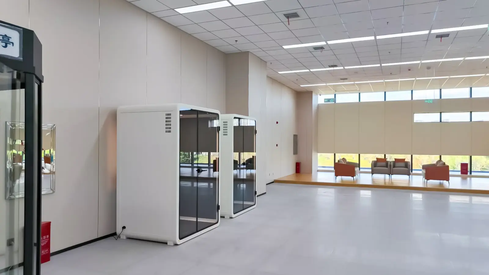 Two white acoustic pods installed beside a seating area in a spacious public building