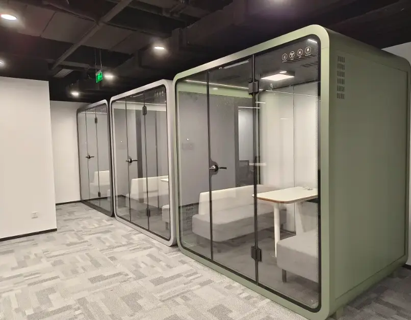 Green acoustic meeting pods with glass doors, tables and seating in a modern office