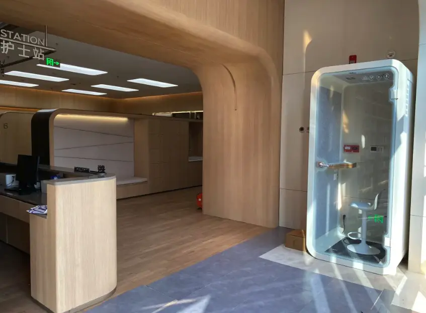 Single-person acoustic pod beside a hospital reception and nurses’ station