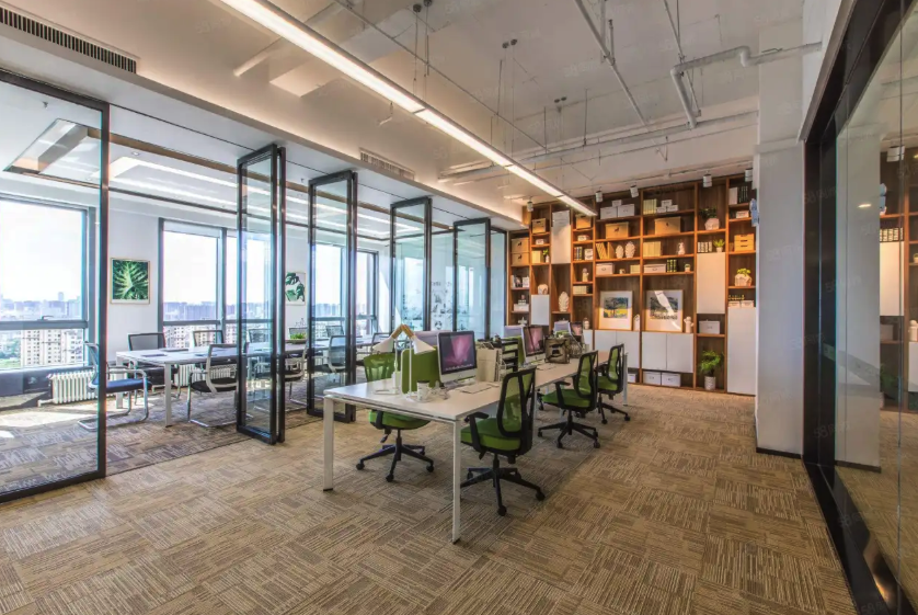 A bright modern open-plan high-rise office has a long white desk with green chairs, a glass-walled meeting room, and wooden.