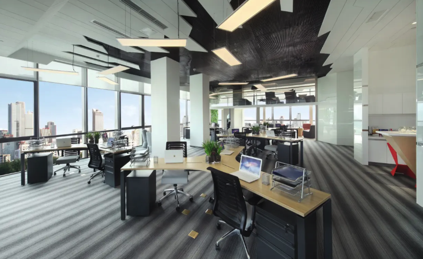 A bright modern open-plan high-rise office has light wood workstations, floor-to-ceiling windows with city views, and a cozy.